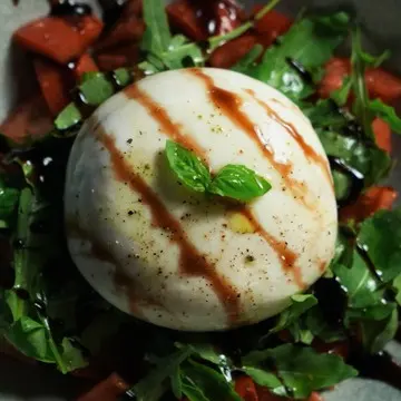 Whole burrata on tomatoes and arugula with balsamic glaze.